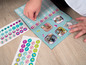 Een kind plakt stickers van medische benodigdheden op een boekje met afbeeldingen van dieren.