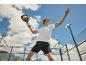 Homme en tenue de padel frappant une balle de padel avec une raquette sur un court extérieur.