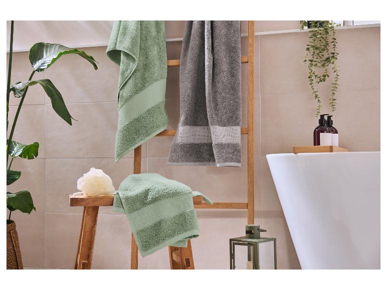 Serviettes vertes et grises sur une échelle en bois dans une salle de bain avec plantes et baignoire.