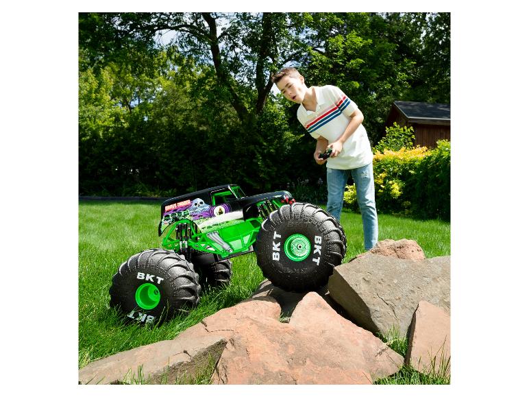 Un garçon contrôle un camion monstre RC Grave Digger sur l'herbe, avec des rochers au premier plan.