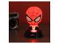 Veilleuse Spiderman illuminée en rouge sur une base noire, avec un appareil photo flou en arrière-plan.