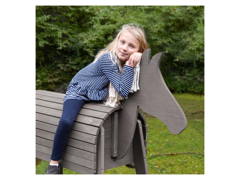 Blond meisje zit op een houten speelpaard buiten.