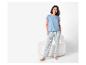 Femme en T-shirt bleu clair et pantalon de pyjama rayé debout près d'une chaise blanche.