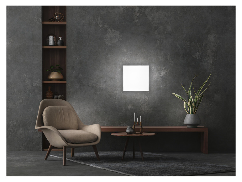 Een moderne stoel, een salontafel en een plant in een donkere kamer met een lichte wandlamp.