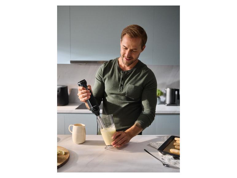 Een man gebruikt de SILVERCREST staafmixer om ingrediënten in een hoge mengbeker te mixen.