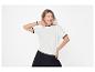 Lachende vrouw in wit T-shirt met ronde hals en zwarte broek, poserend tegen een witte achtergrond.