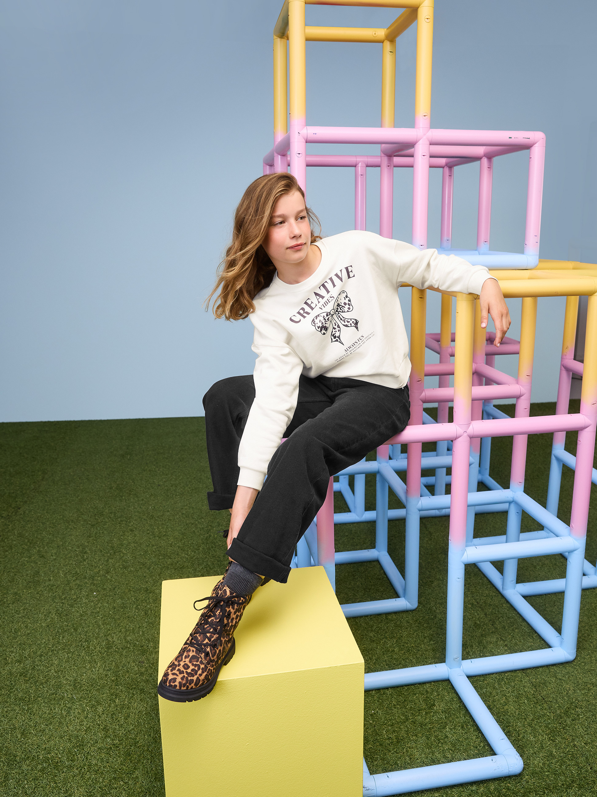 Meisje in witte Creative Vibes-sweater en zwarte broek op een klimrek.