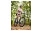 Femme à vélo sur un chemin forestier, vêtue d'une veste rose et d'un casque.