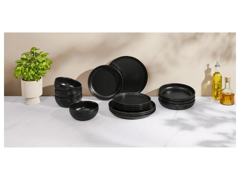 Service de table noir avec assiettes et bols, avec un pot de basilic et des bouteilles d'huile.