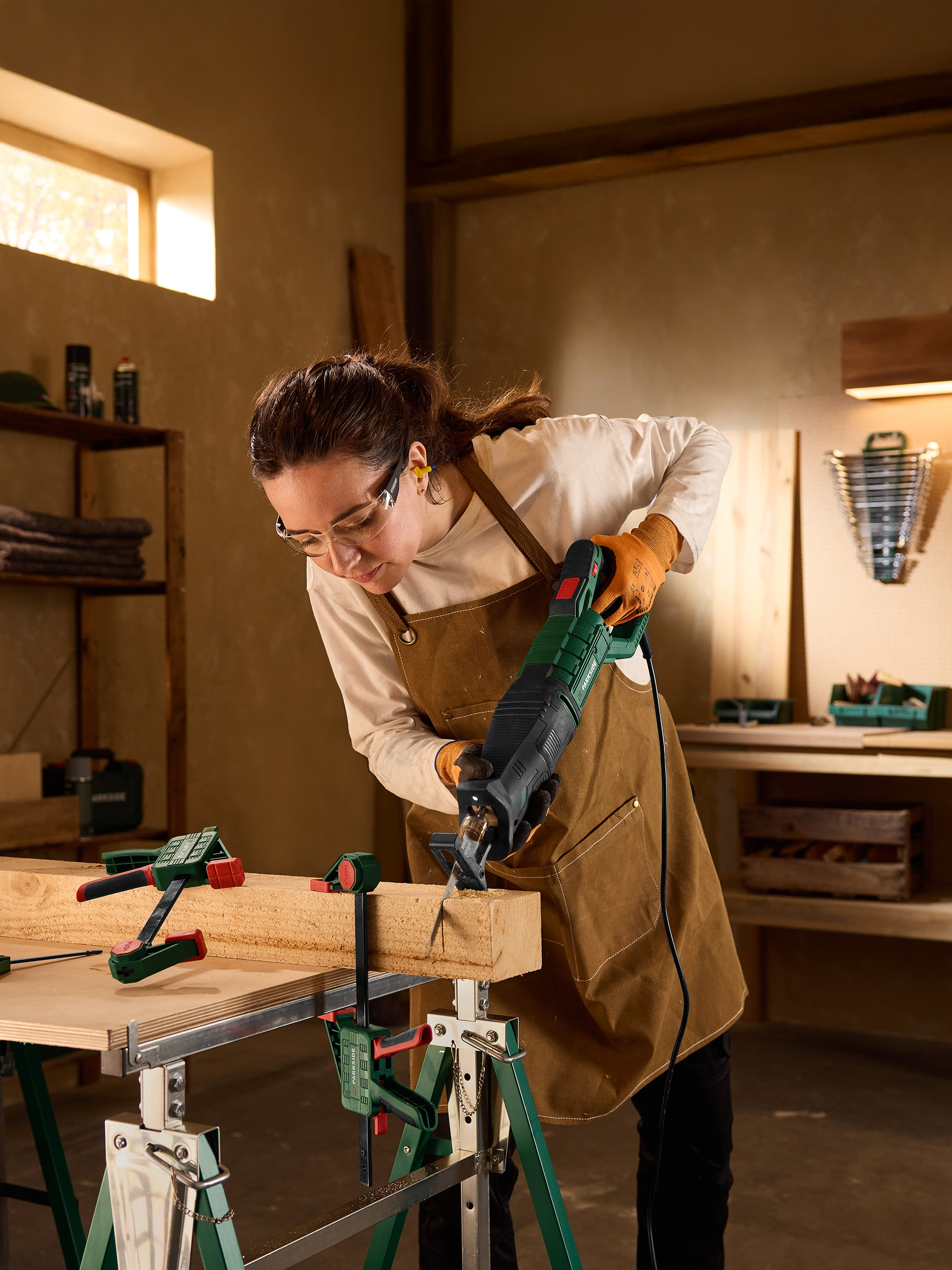 Vrouw gebruikt een reciprozaag om een houten plank te zagen, vastgezet met klemmen.