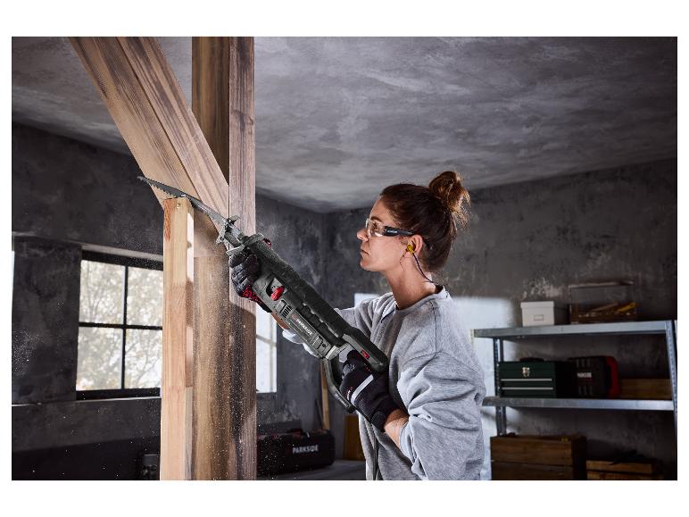 Femme utilisant une scie sabre pour couper du bois, portant des lunettes de sécurité et des bouchons d'oreille.