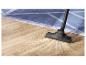 Aspirateur nettoyant la saleté d'un parquet en bois près d'un tapis bleu.