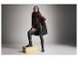 Vrouw in bordeauxrode turtleneck, zwarte leren broek en gewatteerde vest poseert op een houten kist.