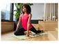 Femme faisant du yoga sur un tapis, vêtue d'un débardeur rouge et d'un legging noir.