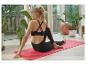Femme en leggings et brassière de sport noirs, faisant du yoga sur un tapis rouge.