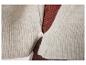 Close-up van een beige gebreid vest met een witte knoop over een bruine geribbelde top.