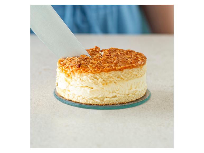 Een mes snijdt een ronde cake met amandeltopping.