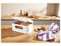 Boîte à pain blanche remplie de produits de boulangerie sur une table en bois, avec un croissant et du beurre.