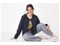 Femme souriante en veste matelassée bleu marine, jean et baskets blanches, assise par terre.
