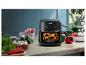 Zwarte airfryer met 180°C instelling en 'RapidAir Technology'-tekst, omringd door verse groenten in de keuken.