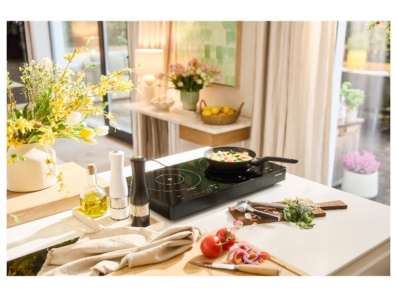 Une plaque à induction noire avec une poêle cuisinant des légumes, entourée d'ingrédients frais.