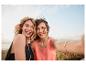 Twee lachende vrouwen in zomerjurkjes bij de zee.