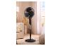 Ventilateur sur pied noir dans un salon avec canapé, lampe et fenêtre.