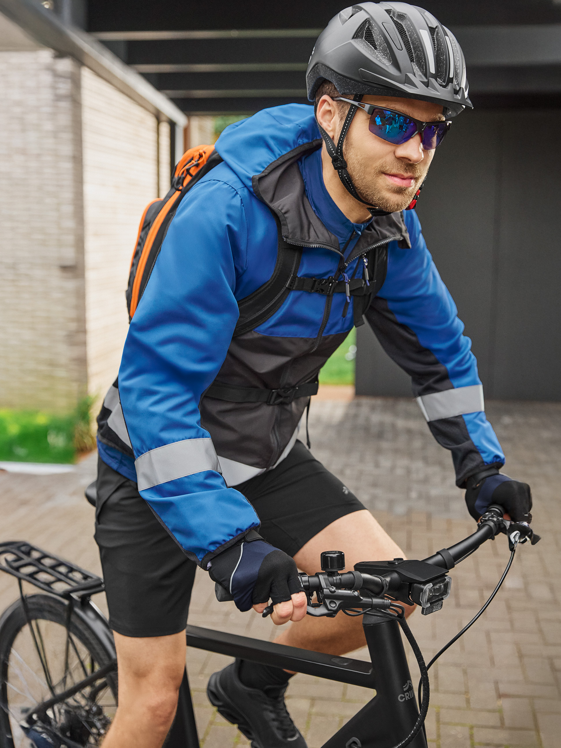 Fietser in blauw-zwart fietsjack, helm en zonnebril, op een zwarte fiets.
