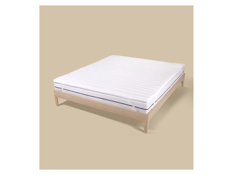 Matelas blanc avec surmatelas sur un cadre de lit en bois clair sur fond beige.
