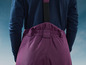 Een vrouw draagt een donkerblauwe trui en een paarse broek met bretels.