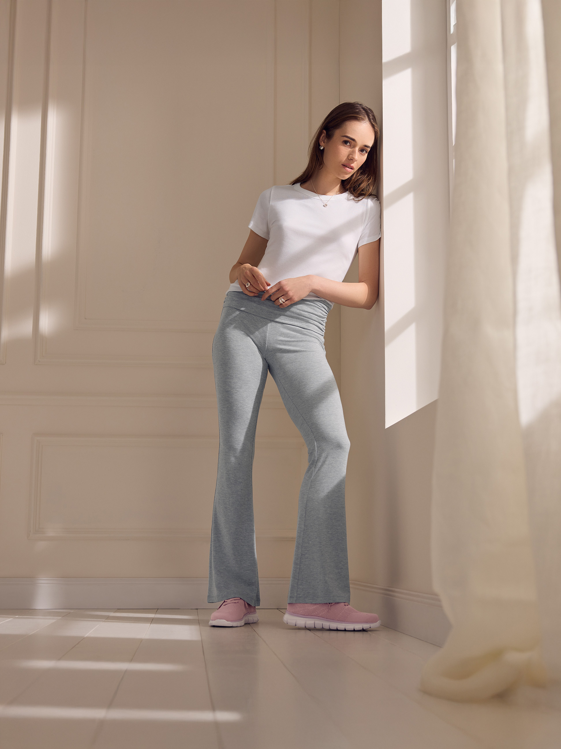Femme en t-shirt blanc et pantalon de jogging gris, appuyée contre un mur