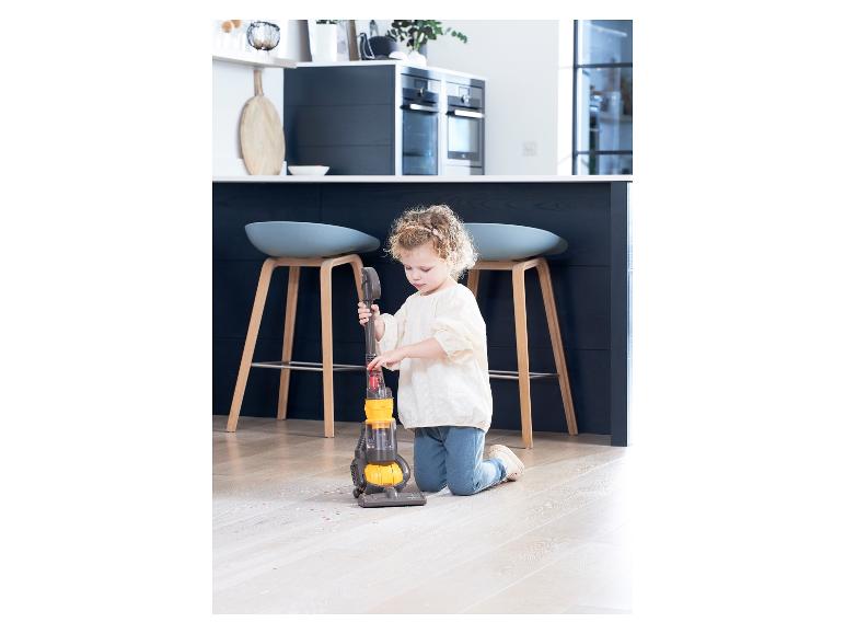 Une petite fille nettoie le sol avec un aspirateur jouet Dyson.