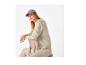 Vrouw met bruine pet en beige sweatshirt zittend op een stoel