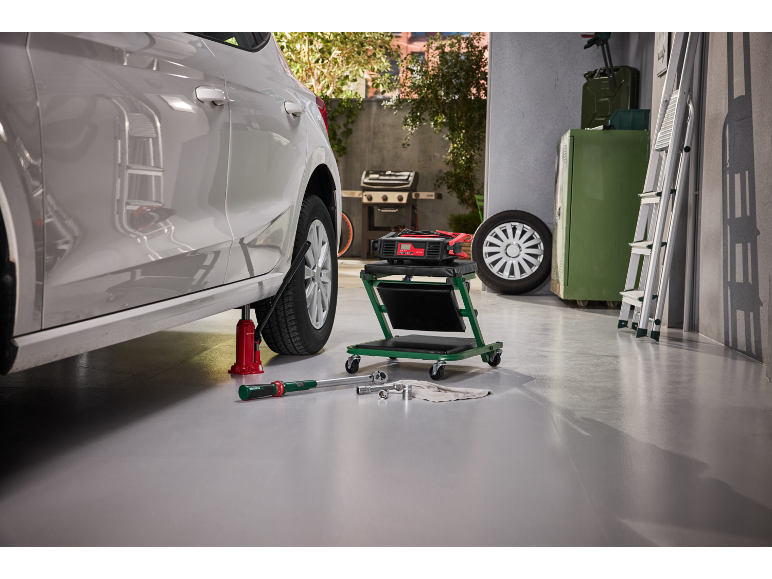 Auto op krik met gereedschap, lader en rolwagen in garage.