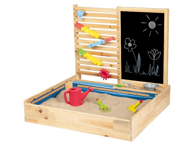 Een houten zandbak met een waterbaan, een krijtbord en speelgoed.