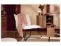 Un fauteuil blanc moelleux avec un plaid rose, à côté d'une table et d'une armoire en bois.