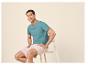 Homme en t-shirt turquoise et short beige assis sur un tabouret.