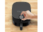 Zwarte airfryer met een hand die de temperatuur aanpast op een houten aanrecht.