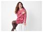 Lachende vrouw in een roze trui-jurk met rode strikken, zittend op een witte kruk.