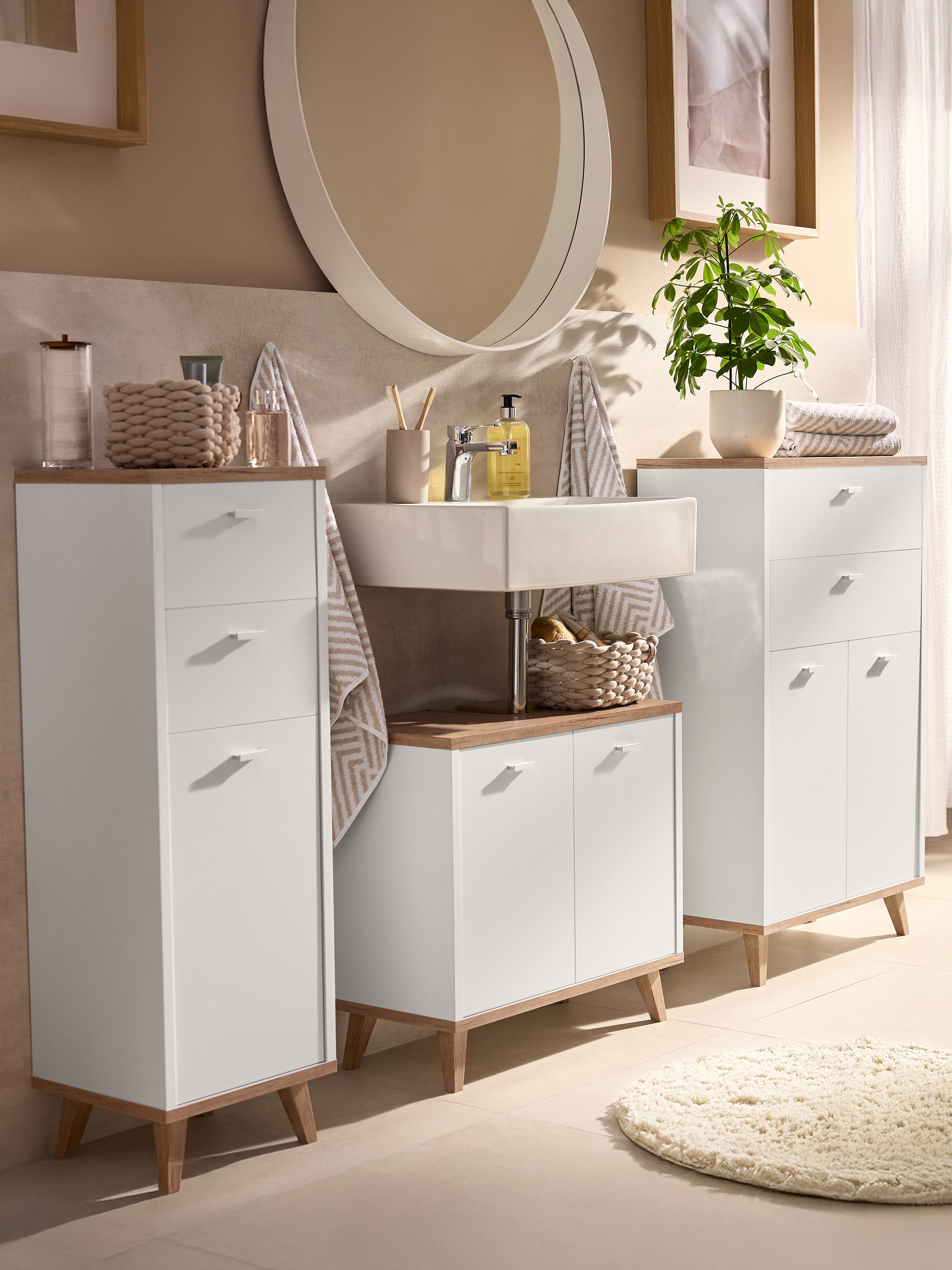 Badkamer met witte kasten, wastafel, spiegel en plant in natuurlijke tinten.