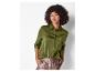 Une femme aux cheveux bouclés portant une chemise verte en satin boutonnée et un pantalon métallique.