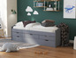 Un lit gris avec rangement, un tapis et un oreiller.