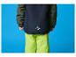 Een kind in een donkerblauwe ski-jas en neon-groene skibroek.