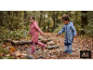 Enfants en combi-pantalon de pluie et bottes en caoutchouc jouant dans une flaque en forêt.