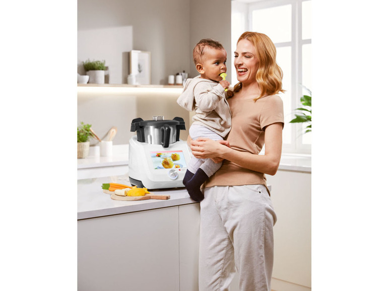 Een moeder houdt haar kind vast in de keuken, naast een witte keukenmachine.