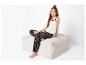 Fille en pantalon de pyjama noir à fleurs et débardeur blanc assise sur un pouf.