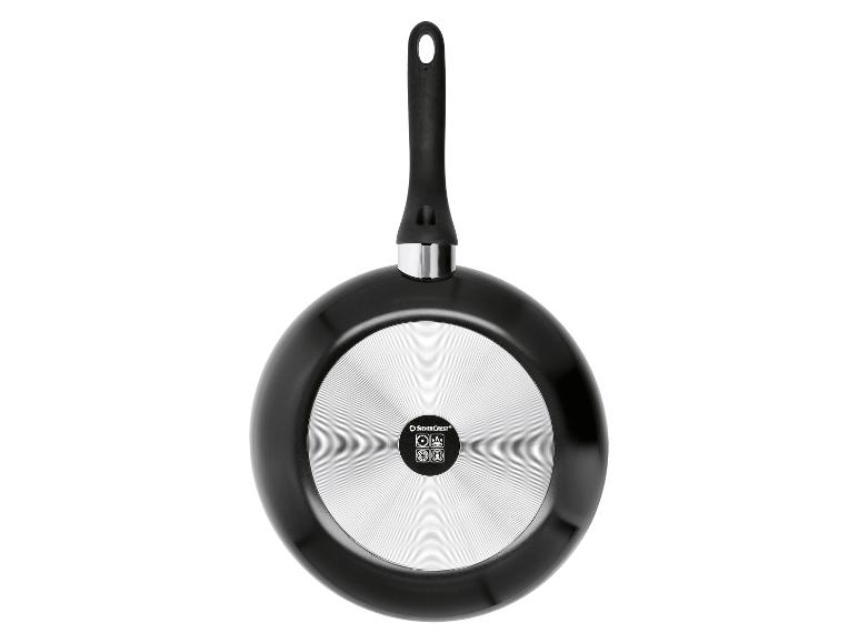 Onderkant van een zwarte koekenpan met metalen bodem en zwart handvat.
