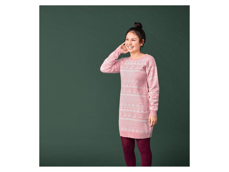 Une femme portant un pull de Noël rose avec des rennes et des flocons de neige.