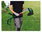 Personne en tenue de travail assemblant un coupe-bordure électrique vert dans un jardin.