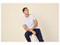 Homme en t-shirt blanc et pantalon bleu assis sur un tabouret.